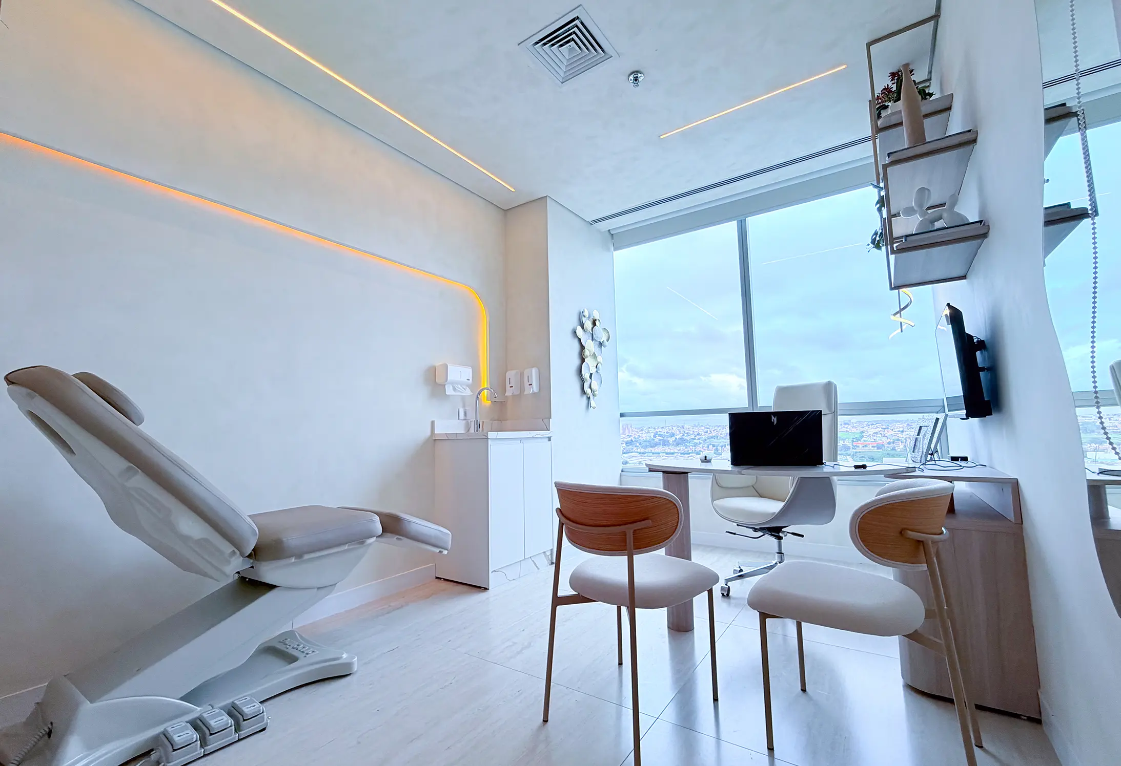 Sala de consulta médica clara e moderna com cadeira reclinável, duas cadeiras para pacientes, mesa com computador e janela grande com vista da cidade.